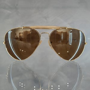 May include: Gold aviator sunglasses with brown lenses. The sunglasses have a classic design and are in good condition.