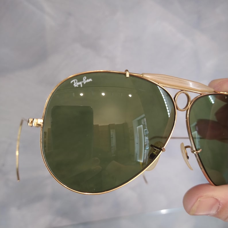 May include: Gold-tone aviator sunglasses with green lenses and a Ray-Ban logo on the frame.