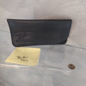 May include: Black leather Ray-Ban Wayfarer sunglasses case with the Ray-Ban logo embossed on the front. A yellow microfiber cleaning cloth with the Ray-Ban logo is also included.