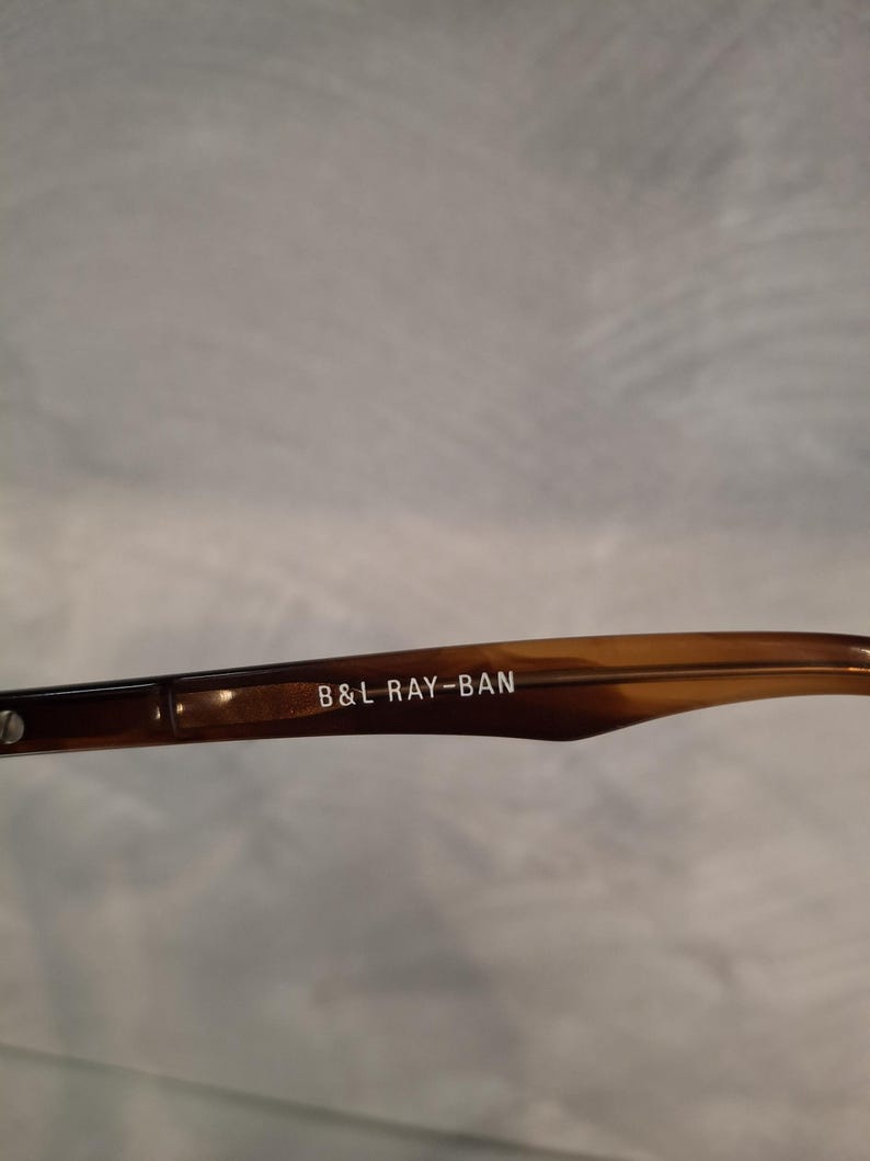 May include: Close-up of a brown and tan Ray-Ban eyeglass arm. The text "B&L RAY-BAN" is printed in white on the arm. The arm has a tortoiseshell pattern.