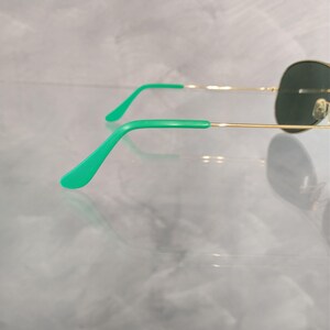 Op de afbeelding: Gouden aviator zonnebril met groene pootjes. De zonnebril heeft donkergroene glazen.