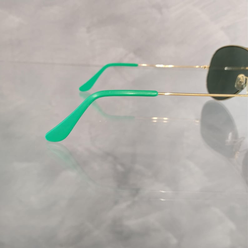 Op de afbeelding: Gouden aviator zonnebril met groene pootjes. De zonnebril heeft donkergroene glazen.