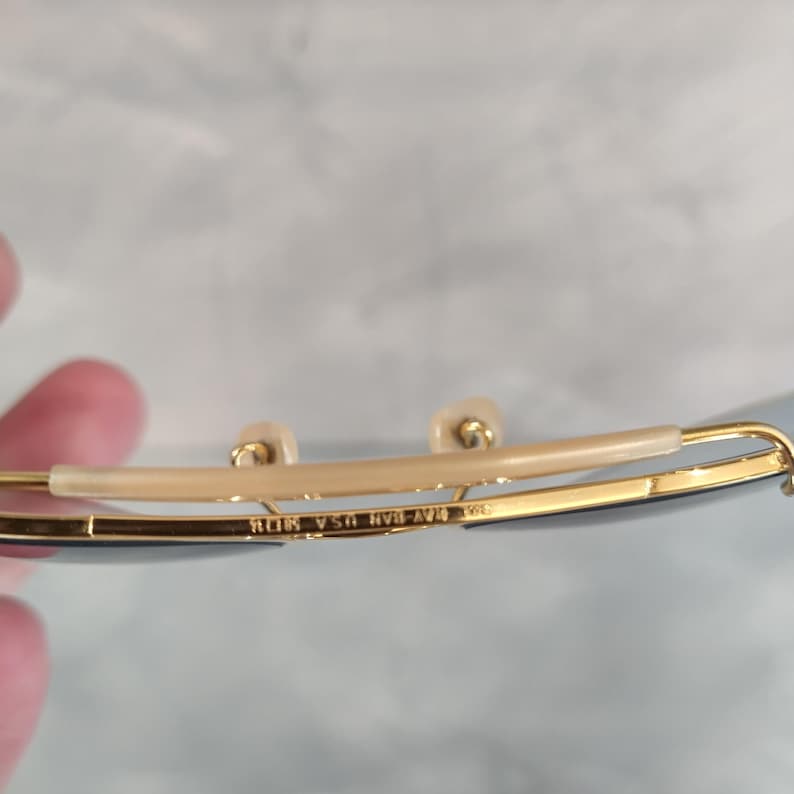 May include: Close-up of the inside of a pair of gold-rimmed sunglasses with the text "Ray-Ban  USA  RB-AV1  58□14  140" engraved on the frame.