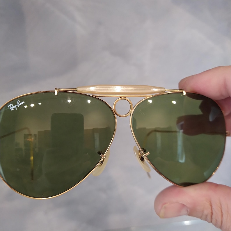May include: Gold-tone aviator sunglasses with green lenses and a Ray-Ban logo on the left lens.