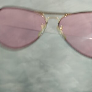 Op de afbeelding: Een gouden aviator zonnebril met roze glazen.