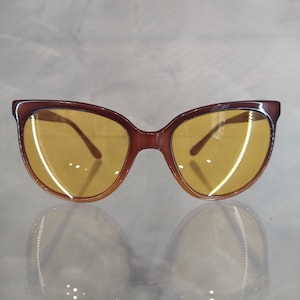 May include: Brown cat-eye sunglasses with yellow lenses. The sunglasses have a classic design and are perfect for a stylish look.
