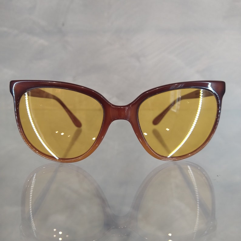 May include: Brown cat-eye sunglasses with yellow lenses. The sunglasses have a classic design and are perfect for a stylish look.