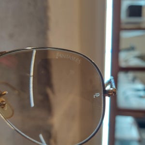 Puede incluir: Primer plano de una gafas de sol aviador marrones con la palabra "FantasEyes" grabada en la lente.