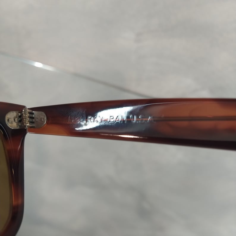 May include: Close-up of the brown plastic arm of a pair of sunglasses with the text "Ray-Ban USA" embossed on the arm.