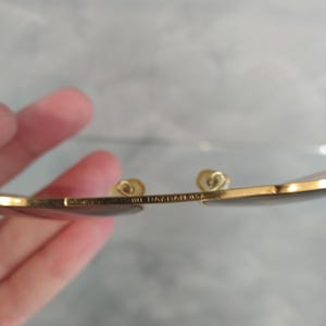 Puede incluir: Primer plano del marco de metal dorado de unas gafas de sol. El marco tiene el texto "Ray-Ban USA" grabado.