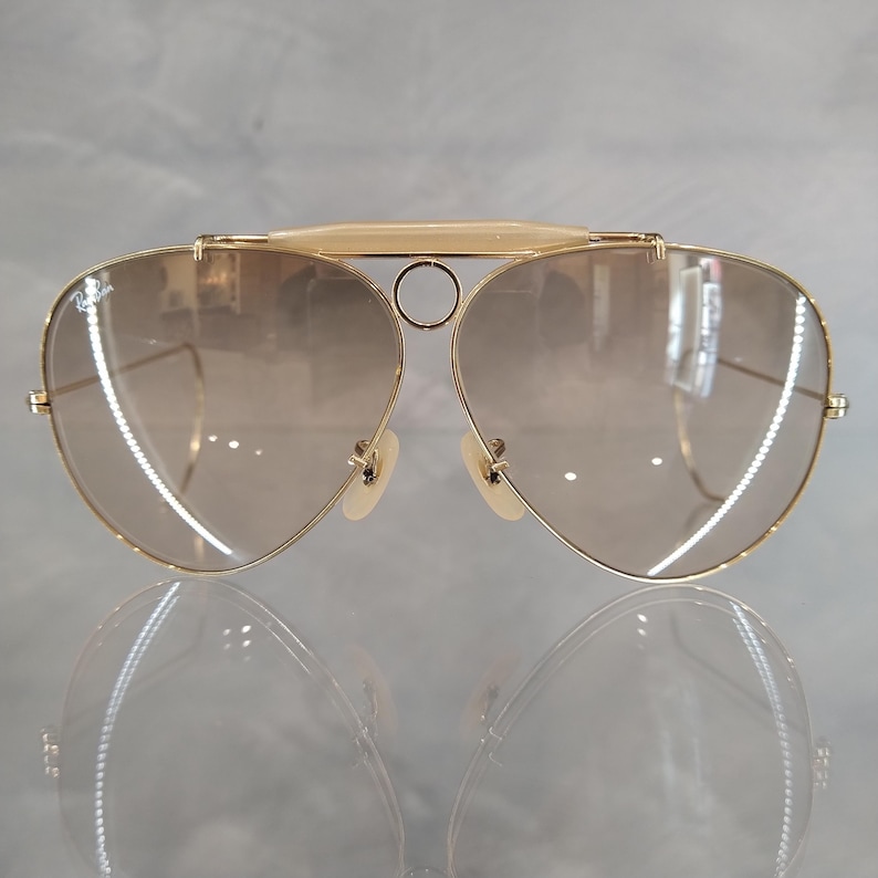 May include: Gold aviator sunglasses with brown gradient lenses. The sunglasses have a metal frame and a double bridge.
