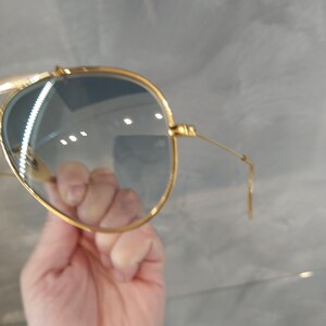 May include: Gold aviator sunglasses with blue gradient lenses. The sunglasses are being held in a hand.