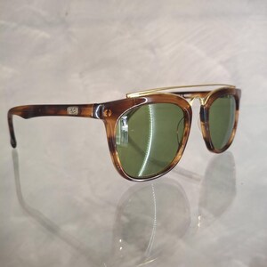 May include: Sunglasses with a brown tortoiseshell frame and green lenses. The sunglasses have a gold-colored metal bridge and arms. The lenses are a dark green color, and the frame has a classic, retro design.