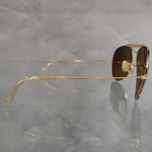 May include: Gold aviator sunglasses with brown lenses. The sunglasses are shown from the side, with the arms extended.