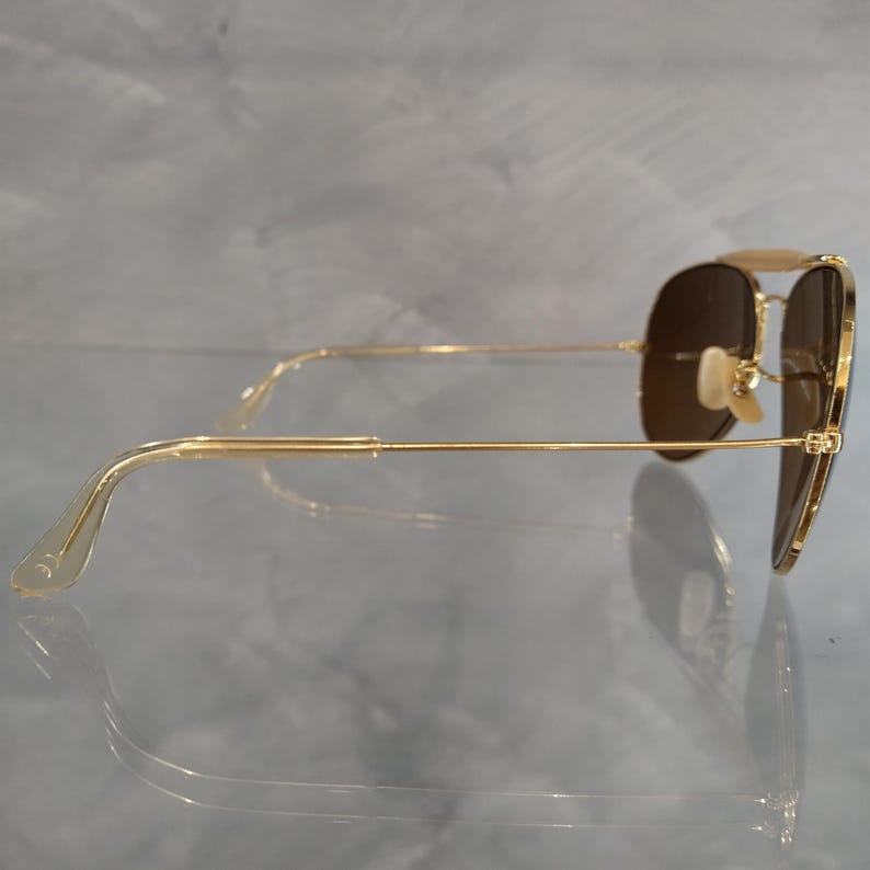 May include: Gold aviator sunglasses with brown lenses. The sunglasses are shown from the side, with the arms extended.