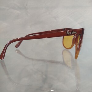 May include: Brown plastic sunglasses with yellow lenses. The sunglasses have the Ray-Ban logo on the right temple.