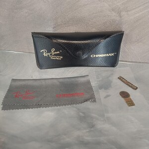 May include: Black leather Ray-Ban sunglasses case with the text "Ray-Ban Driving Series" and "CHROMAXX" in gold lettering. The case is accompanied by a gray microfiber cleaning cloth with the Ray-Ban logo and a small gold sticker with the text "CHROMAXX".