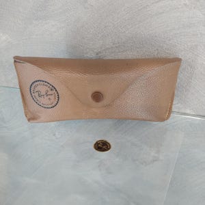 May include: A brown leather case for sunglasses with a Ray-Ban logo embossed on the front.