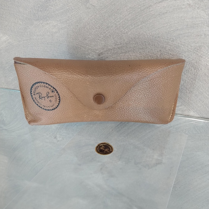 May include: A brown leather case for sunglasses with a Ray-Ban logo embossed on the front.