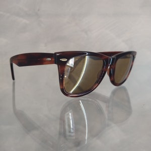 May include: Brown tortoiseshell sunglasses with brown lenses. The sunglasses are reflected in a shiny surface.