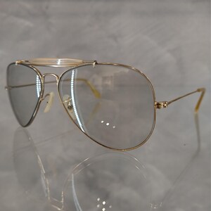May include: Gold aviator sunglasses with clear lenses and a thin metal bridge.