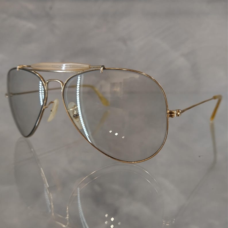 May include: Gold aviator sunglasses with clear lenses and a thin metal bridge.