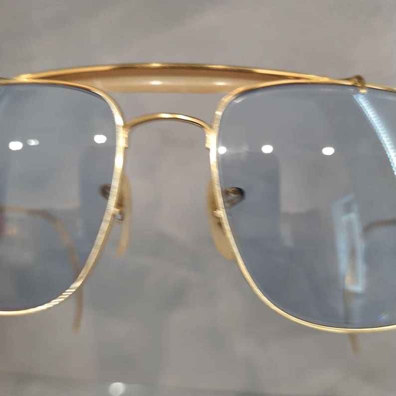 Puede incluir: Gafas de sol aviador doradas con lentes azules. Las gafas tienen un dise&ntilde;o cl&aacute;sico con un fino marco de metal.