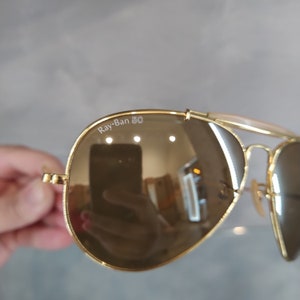 May include: Gold aviator sunglasses with brown lenses and a Ray-Ban 50 inscription on the frame.