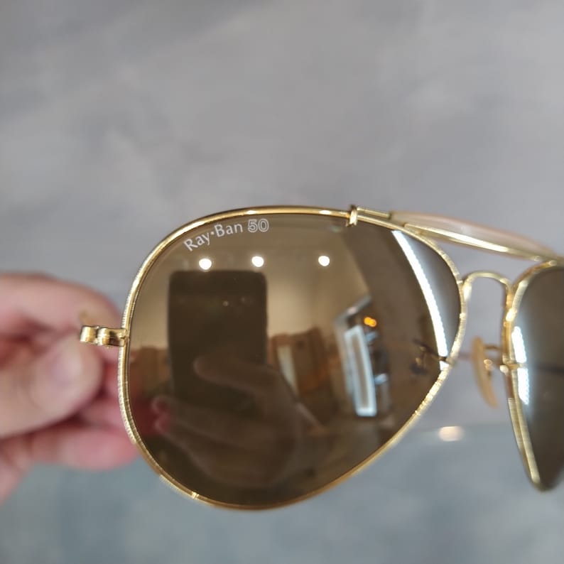 May include: Gold aviator sunglasses with brown lenses and a Ray-Ban 50 inscription on the frame.