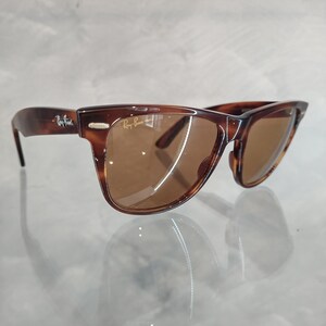 May include: Brown tortoise shell Ray-Ban Wayfarer sunglasses with brown lenses. The sunglasses are on a white surface.