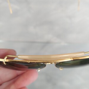 May include: Gold-tone aviator sunglasses with green lenses and a brown plastic nose bridge.