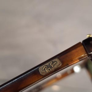 May include: Close-up of Ray-Ban sunglasses with a tortoiseshell pattern. The frame is brown and the Ray-Ban logo is visible on the temple. The glasses have a classic design.