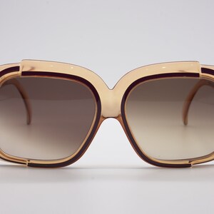 May include: A pair of brown and gold oversized sunglasses with a square frame. The sunglasses have a gradient lens that fades from dark to light.