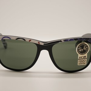 Puede incluir: Gafas de sol Ray-Ban negras con montura plateada y lentes verdes. La montura tiene un patr&oacute;n colorido con el logotipo de Ray-Ban y el texto "G-15 Lens" en el lado derecho.