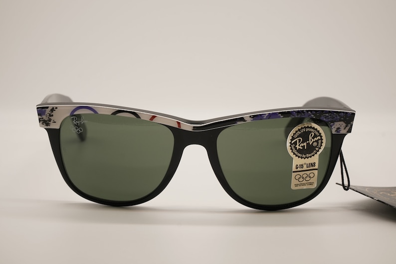 Puede incluir: Gafas de sol Ray-Ban negras con montura plateada y lentes verdes. La montura tiene un patr&oacute;n colorido con el logotipo de Ray-Ban y el texto "G-15 Lens" en el lado derecho.