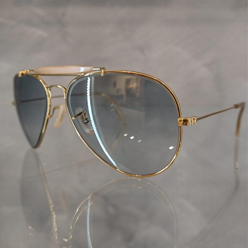 May include: Gold aviator sunglasses with a white bar across the bridge and blue gradient lenses.