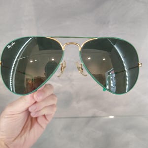 Op de afbeelding: Groene aviator zonnebril met gouden montuur. De glazen zijn gespiegeld en reflecteren de omgeving.