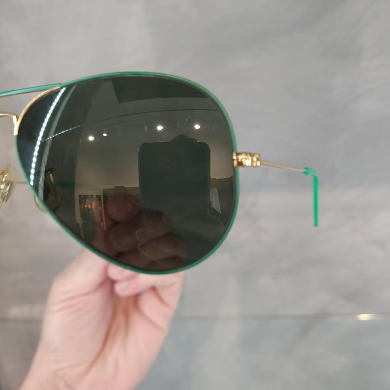 Op de afbeelding: Groene aviator zonnebril met gouden accenten en groene pootjes. De zonnebril heeft donkergroene glazen.