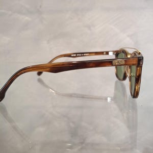 May include: Brown and tortoise shell sunglasses with green lenses. The sunglasses have a classic design with a rectangular frame and a Ray-Ban logo on the temple. The arms are a darker brown color.