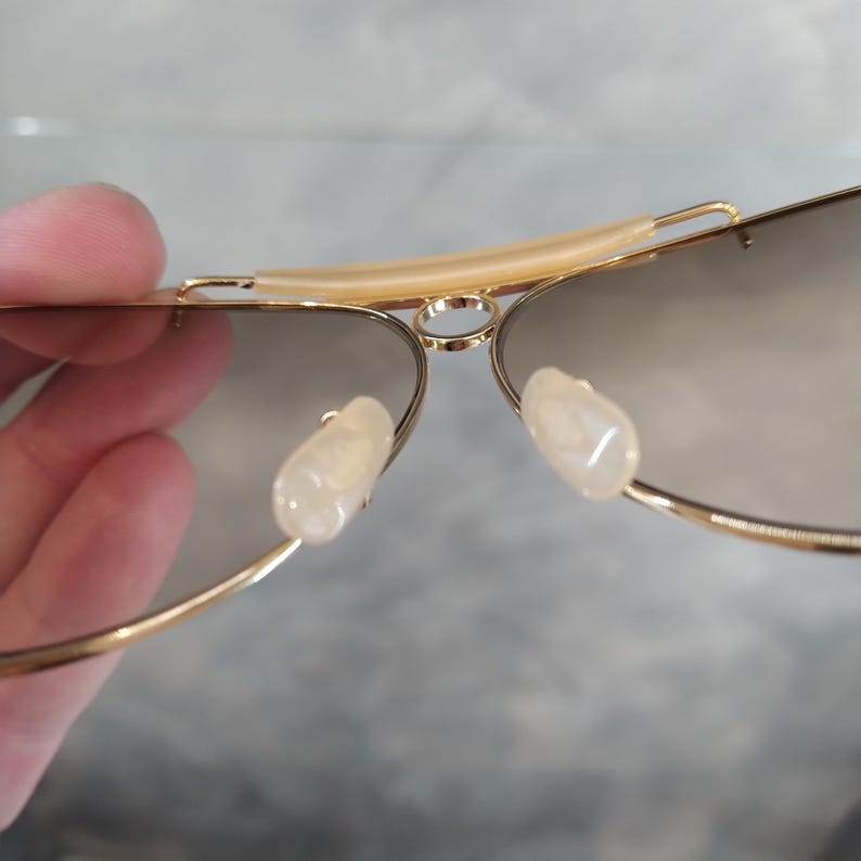 May include: Gold aviator sunglasses with brown lenses and white plastic nose pads.