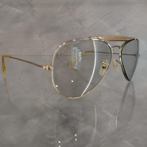 May include: Gold aviator sunglasses with clear lenses and a gold metal frame.