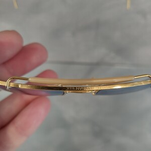 Puede incluir: Primer plano del marco de metal dorado de unas gafas de sol. El marco tiene un puente nasal de pl&aacute;stico marr&oacute;n y el texto "B&L RAY-BAN USA" est&aacute; grabado en el marco.