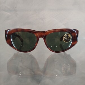 Peut inclure: Lunettes de soleil en écaille de tortue marron avec des verres verts et un logo Ray-Ban sur la lentille droite.