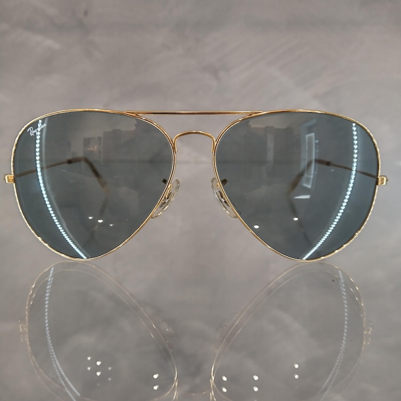 Puede incluir: Gafas de sol aviador doradas con lentes espejados gris oscuro.