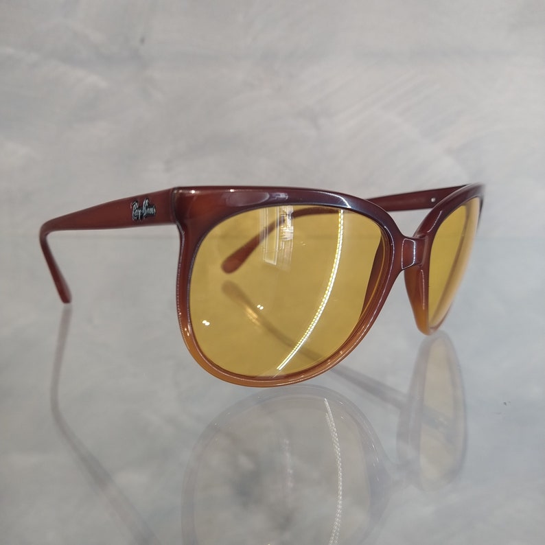 May include: Brown plastic sunglasses with yellow lenses. The sunglasses have a Ray-Ban logo on the side.
