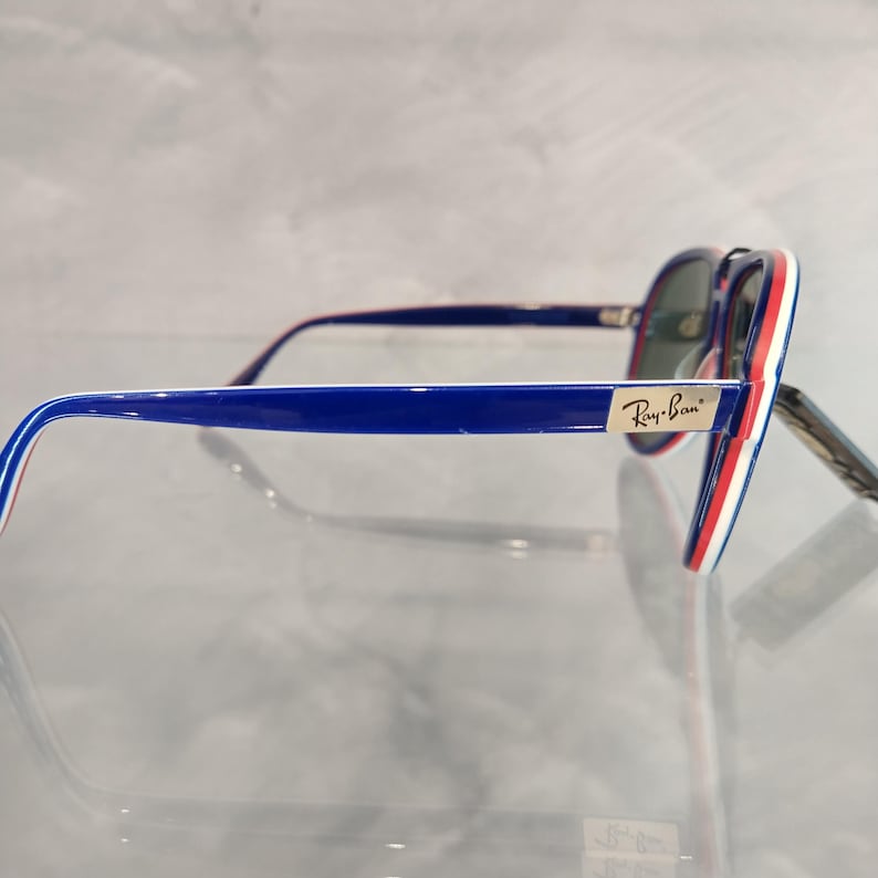 May include: Blue and red aviator sunglasses with white accents. The sunglasses have a Ray-Ban logo on the side.