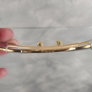 May include: Close-up of the underside of a pair of gold-tone glasses. The glasses have a thin metal frame and clear lenses. The inscription "W.G. & Co. 1/10 12K GF" is visible on the frame.