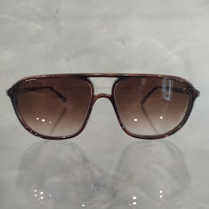 Op de afbeelding: Bruine aviator zonnebril met een donkerbruin verlooplens. De zonnebril heeft een metalen balk over de neusbrug.