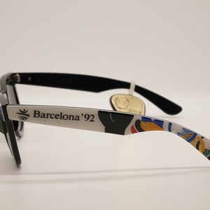 K&ouml;nnte beinhalten: Schwarze Sonnenbrille mit silbernem Rahmen und einem bunten olympischen Design. Der Rahmen tr&auml;gt den Schriftzug "Barcelona '92".