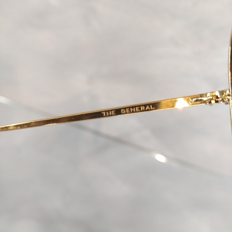 May include: Close-up of the gold-colored arm of a pair of glasses with the words "THE GENERAL" engraved on the arm.
